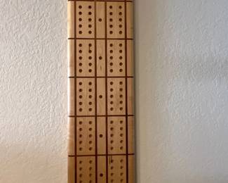 Handcrafted wall-hanging wooden cribbage board featuring inlaid grid lines and top peg storage slots.