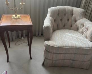 Vintage tufted barrel armchair with pastel striped upholstery alongside a cabriole-leg wooden side table and two-light brass table lamp.