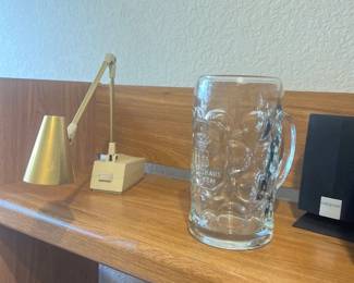 Vintage brass adjustable desk lamp alongside a Hofbräuhaus München dimpled glass beer stein on a wooden shelf.