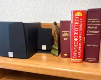 Collection of reference books, including Random House Webster's College Dictionary and Dorland's Illustrated Medical Dictionary, displayed alongside small computer speakers on a light oak shelf.