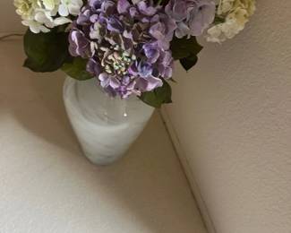 Arrangement of artificial hydrangea stems in purple, lavender, and cream tones set inside a frosted glass vase.