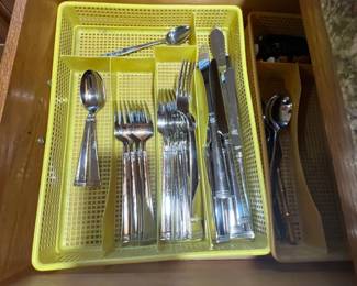 Set of stainless steel flatware organized inside yellow plastic drawer trays, featuring knives, forks, and spoons.