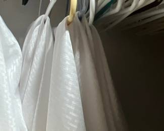 White patterned linens hanging on plastic clothes hangers in a closet.