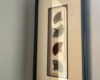 Framed wall art featuring a vertical arrangement of decorative mini folding fans in a dark molded frame.