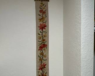 Vintage embroidered bell pull featuring a colorful floral motif and brass hardware hanging on a white wall.