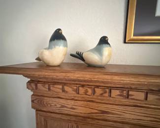 Pair of carved and painted wooden bird figurines displayed on an oak fireplace mantle.
