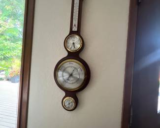 Vintage wood banjo-style weather station featuring a thermometer, clock, barometer, and hygrometer with brass bezel accents.