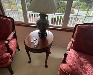 Pair of traditional Queen Anne style armchairs with red patterned upholstery, set beside an oval cherry wood end table topped with a ceramic urn lamp.