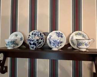 Collection of four vintage porcelain teacups and matching saucers, featuring various blue floral patterns and gold trim, displayed on a wooden shelf.