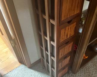 Tall, narrow wooden storage tower featuring five drawers with woven bamboo fronts and open slatted side paneling.