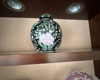 Chinese Famille Noire porcelain ginger jar decorated with hand-painted pink peonies and leafy green vines on a black ground, displayed on a wooden shelf.