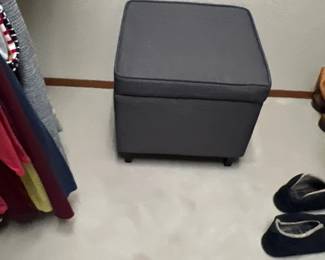 Contemporary dark gray upholstered storage ottoman sitting in a closet floor.
