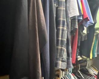 Selection of men's casual clothing hanging in a closet, including plaid button-down shirts, t-shirts, and long-sleeve tops.