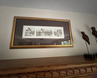 Framed triptych print featuring waterfowl in a gold-finished wood frame, alongside two decorative wooden bird figurines.