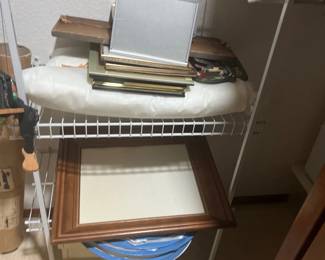 Assorted picture frames, including a large wooden wall frame and various smaller desk and wall frames, stored on closet shelving.