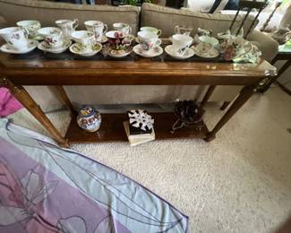Collection of vintage porcelain teacups and saucers arranged on a wooden console table with a lower shelf.