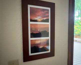 Framed wall art featuring three stacked landscape photographs of a sunset in a dark wood frame with white matting.