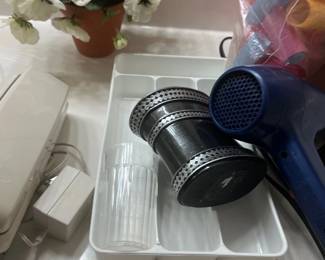 Collection of bathroom and household accessories, including a blue hair dryer, a plastic drawer organizer, a decorative cup, and a potted artificial plant.