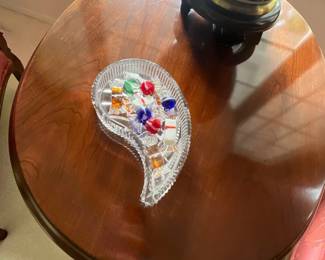 Vintage paisley-shaped cut crystal candy dish filled with decorative glass candies, displayed on an oval cherry wood side table.