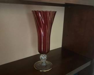 Tall ruby red blown glass vase featuring a swirl pattern, twisted clear glass knop, and round foot rimmed in gold.