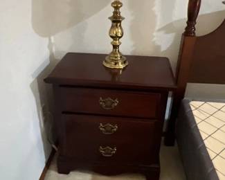 Traditional dark wood nightstand with brass hardware, featuring a polished brass table lamp with a pleated shade.
