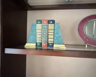 Set of three Reader's Digest Condensed Books held by faux-marbled bookends on a wooden shelf alongside a pair of brass candlesticks and a decorative plate.