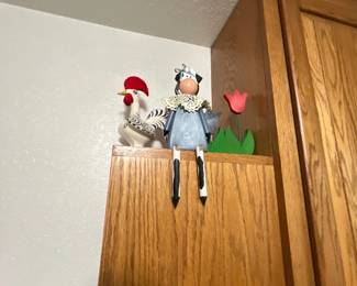 Collection of country-style decorative items, including a ceramic rooster figurine, a wooden shelf-sitter cow, and a wooden tulip cutout, displayed atop an oak cabinet.