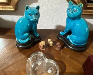 Pair of vintage turquoise glazed ceramic cat figurines on wooden stands, accompanied by three miniature monkey figurines and an etched heart-shaped glass trinket dish.