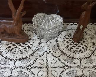 Heart-shaped lead crystal trinket box flanked by carved wooden antelope figurines, displayed on a lace table runner.