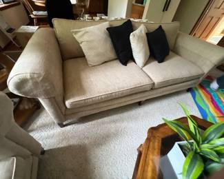 Contemporary beige upholstered sofa featuring rolled arms and dark tapered wooden legs, styled with contrasting black and patterned throw pillows.