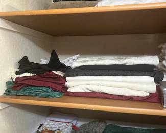 Assorted household linens, towels, table runners, and oven mitts neatly stacked on wooden closet shelves.