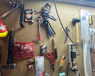 A pegboard wall organized with an assortment of hand tools, including hammers, pliers, hex keys, safety glasses, and a power strip.