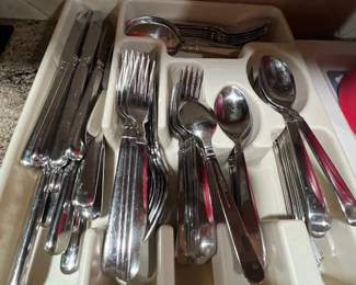 Large set of modern stainless steel flatware, including knives, forks, and spoons, organized in a plastic drawer tray.