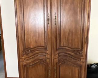 French Provincial style carved wooden armoire featuring double panel doors with ornate brass hardware and cabriole legs.