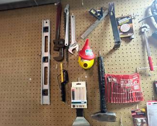 Assortment of hand tools hung on a pegboard wall, including pipe wrenches, adjustable wrenches, levels, a hammer, funnels, and a hex key set.