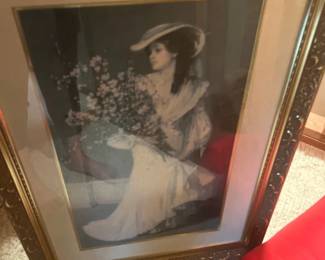 Framed vintage art print depicting a Victorian-style woman in a wide-brimmed hat holding a bouquet of flowers. Housed behind glass in a decorative ornate metallic frame with double matting.