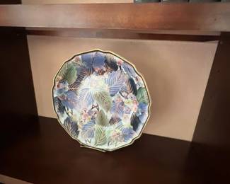 Vintage Japanese chokin decorative plate featuring detailed floral and leaf motifs with gold accents, displayed on a dark wood bookcase shelf.