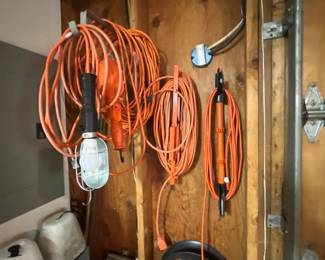 Assortment of heavy-duty orange extension cords, cord organizers, and a cage-protected drop light hanging on a workshop wall.