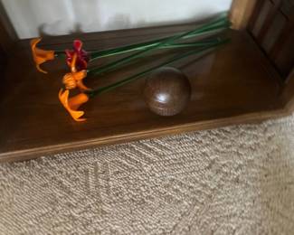 Collection of vibrant blown glass flower stems in orange and red hues, displayed in a wooden rack alongside a dark wooden sphere.