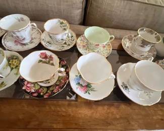 Collection of assorted vintage porcelain tea cups and matching saucers featuring floral motifs and gold rim details displayed on a table.