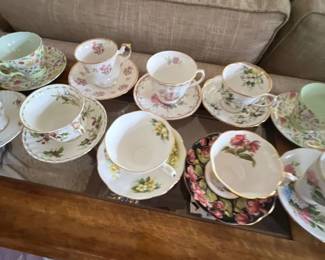 Collection of assorted vintage floral porcelain teacups and matching saucers displayed on a glass-top table.