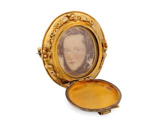 1051 A Gold and Enamel Mourning Locket Centering a blue enamel buckle design that opens to a drawn portrait, finished with a compartment featuring a lock of blonde hair  Measures: 1 3/4 x 1 3/8 in. 22.0 grams gross Estimate: $1,500 - $2,000
