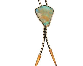 1179 A 14K Gold and Boulder Opal Bolo Tie Centering an organic boulder opal finished with a gold and black leather woven cord, finished with gold plated terminations  Bolor Slide: 2 x 1 3/4 in., Cord: 40 in. 54.7 grams gross Estimate: $1,500 - $2,000