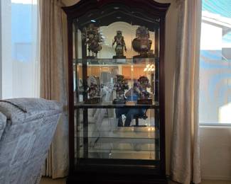 large traditional-style curio display cabinet with a dark cherry/mahogany-tone finish, arched crown, glass shelving, mirrored interior, and a locking glass door with key.