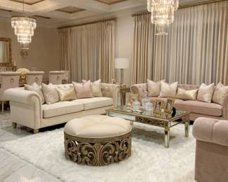Cream tufted sofas, carved living room seating and a round upholstered ottoman for a traditional formal sitting room.