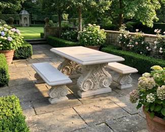 Decorative outdoor dining table with matching garden benches, carved pedestal furniture and formal patio seating.