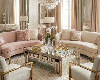 Curved blush pink and cream sofas with gold-tone coffee tables, upholstered accent seating and modern glam living room decor.