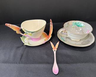 Butterfly Handle Teacup and Saucer with Spoon, Plus Floral Teacup Set A sculpted teacup and saucer with butterfly-wing handles, painted iris accents and a matching butterfly spoon, plus a second cup and saucer with painted leaves and gold trim. A pretty pair for teacup collectors or a tea party display.