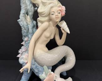 Lladró Porcelain Mermaid on Coral Reef Sculpture A large Lladró porcelain sculpture of a mermaid seated on a blue coral reef, holding a conch shell to her ear, with a flower in her hair, a sculpted fish and sculpted flowers around the base. A showpiece for Lladro collectors and mermaid enthusiasts.