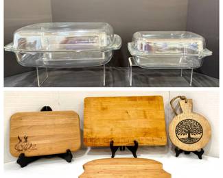 Glass Covered Casserole Dishes and Wood Cutting Board Lot Two clear glass covered casserole or roasting dishes in two sizes, plus four wood cutting boards: a garlic-engraved board, a butcher-block style board, a light wood board with a handle cutout and a round tree-of-life paddle board. Useful everyday kitchen basics.